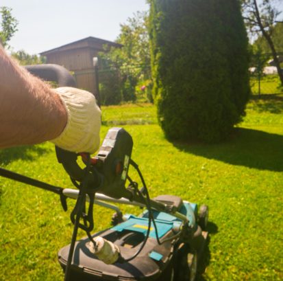 Lawn mover on green grass in modern garden or backyard. Machine for cutting lawns. Gardening care tools and equipment. Process of lawn trimming.