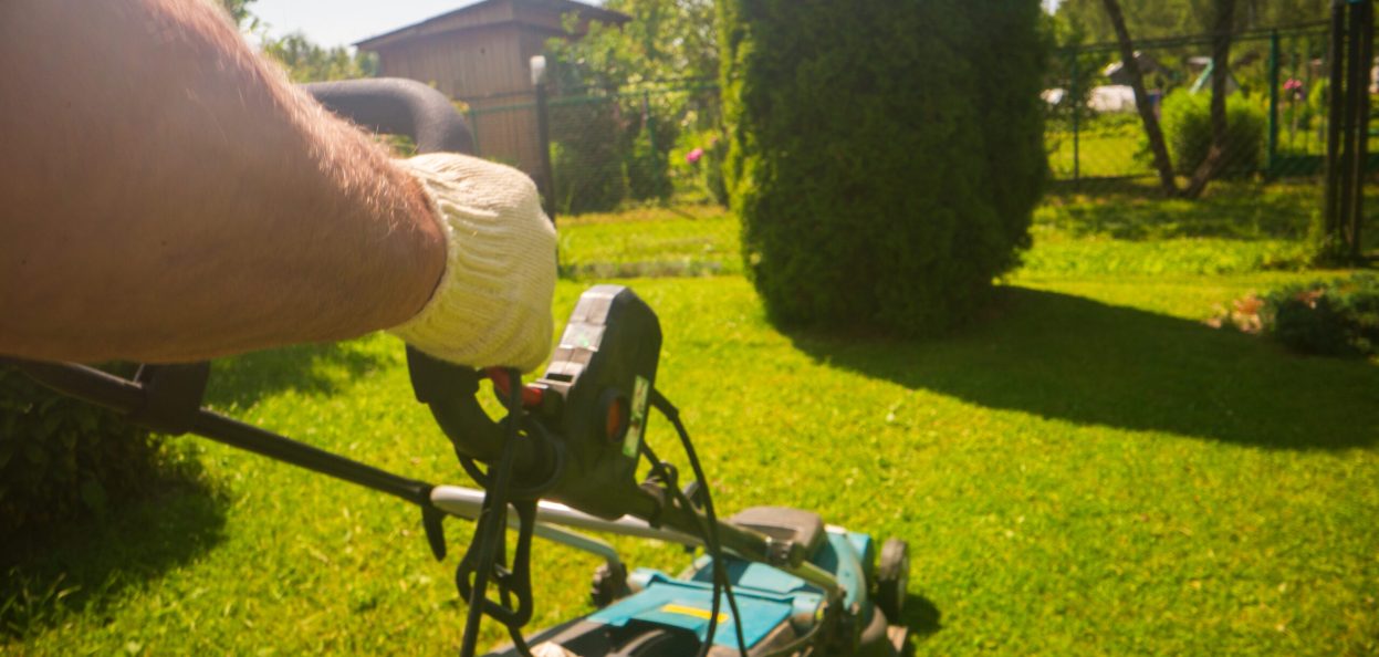 Lawn mover on green grass in modern garden or backyard. Machine for cutting lawns. Gardening care tools and equipment. Process of lawn trimming.